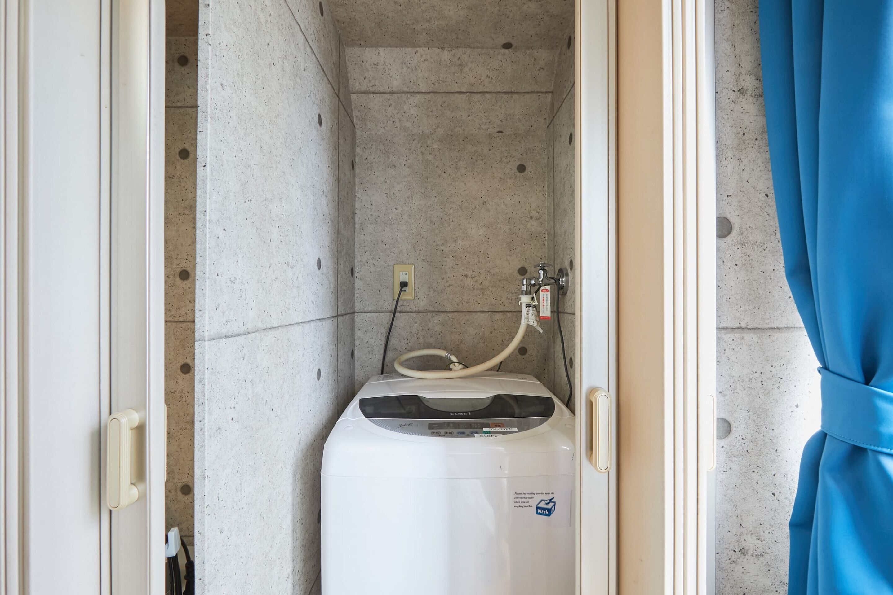 Un baño moderno y compacto con calentador de agua integrado, un enchufe eléctrico a la vista y cortina de ducha.