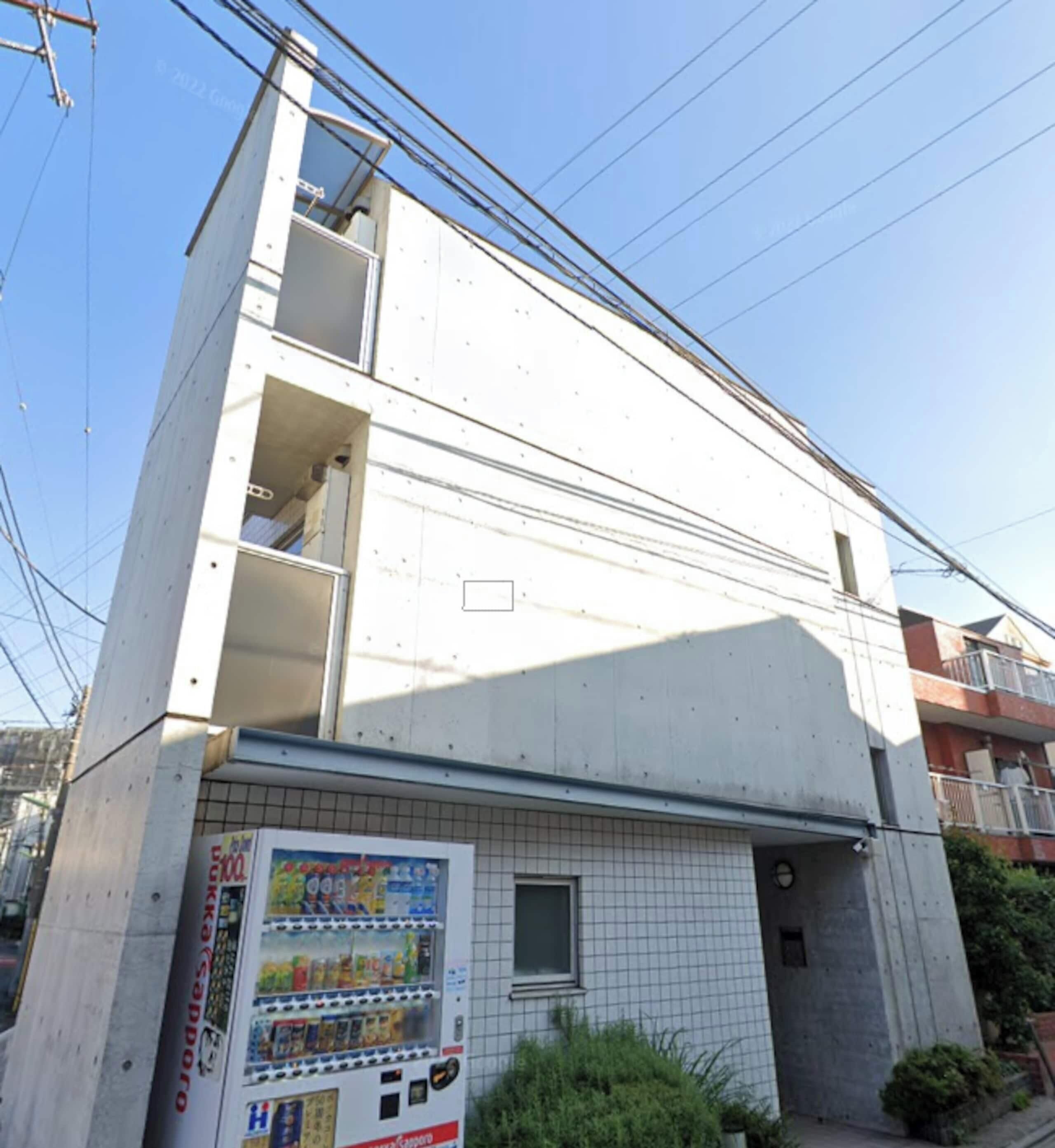 Un edificio de varios pisos con una máquina expendedora en la planta baja, un ventanal visible y un balcón en los pisos superiores.