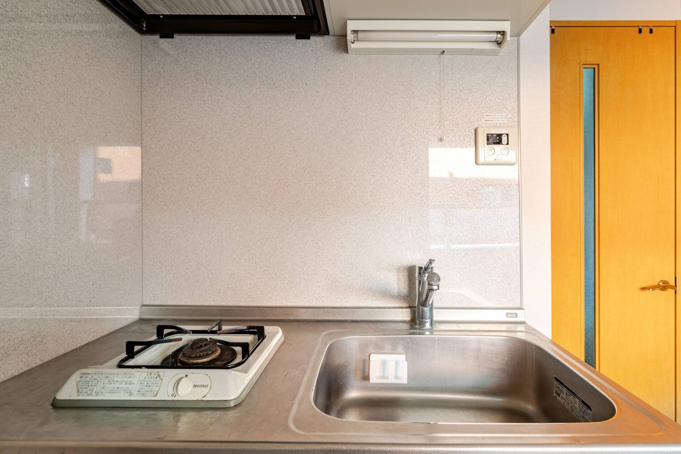 Una cocina con estufa a gas, pileta de acero inoxidable y puerta de madera.