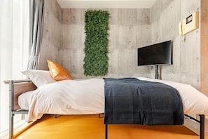 Ein Schlafzimmer mit einem Bett, einem Fernseher, einer Wandpflanze und einer Betonwand.