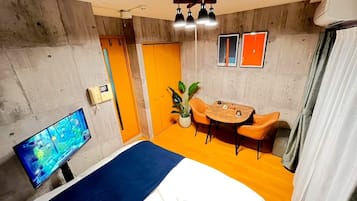 A room with a bed, a desk, a chair, a potted plant, and a television.