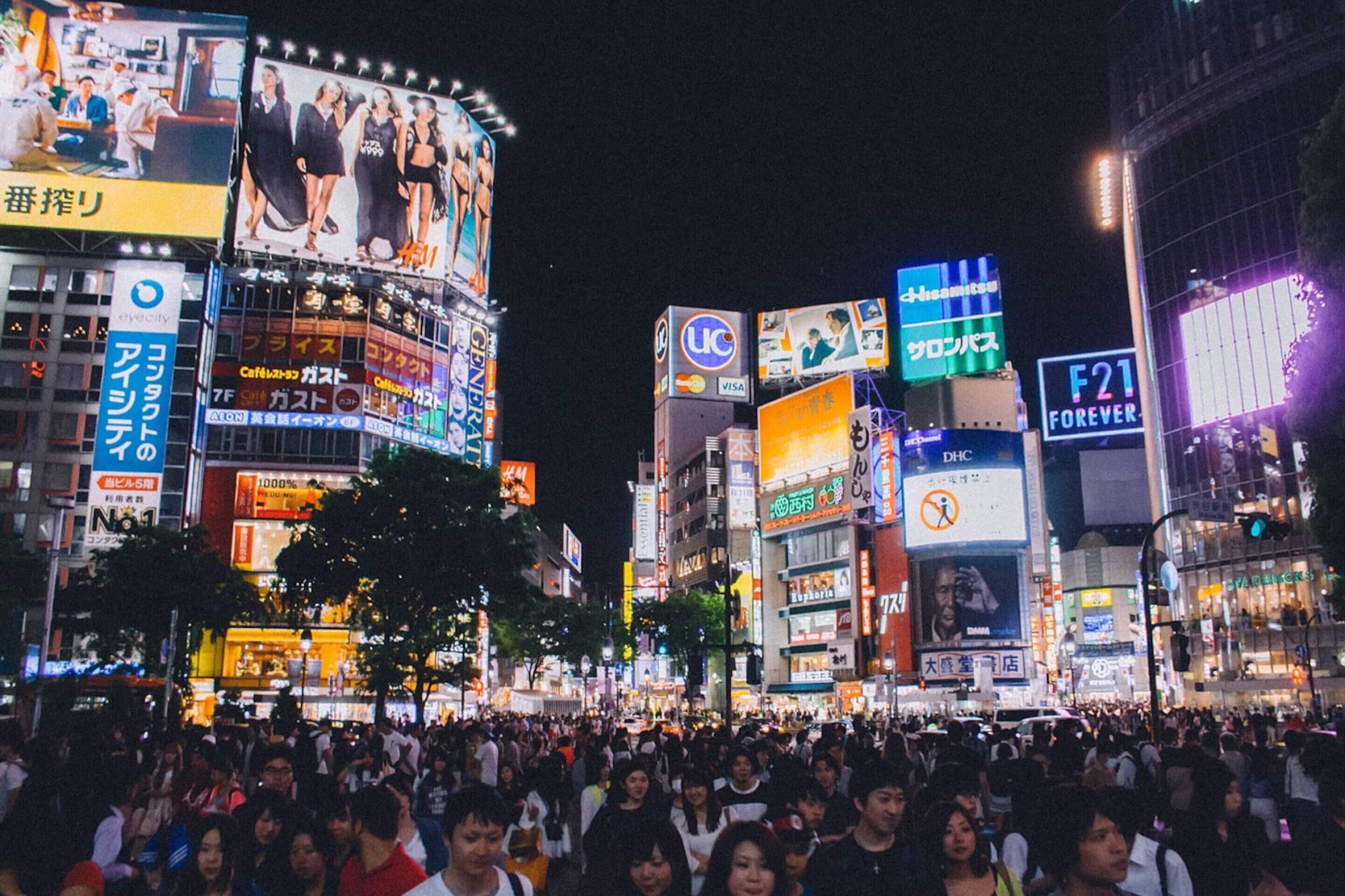 A crowded urban street at night with illuminated billboards and signs.