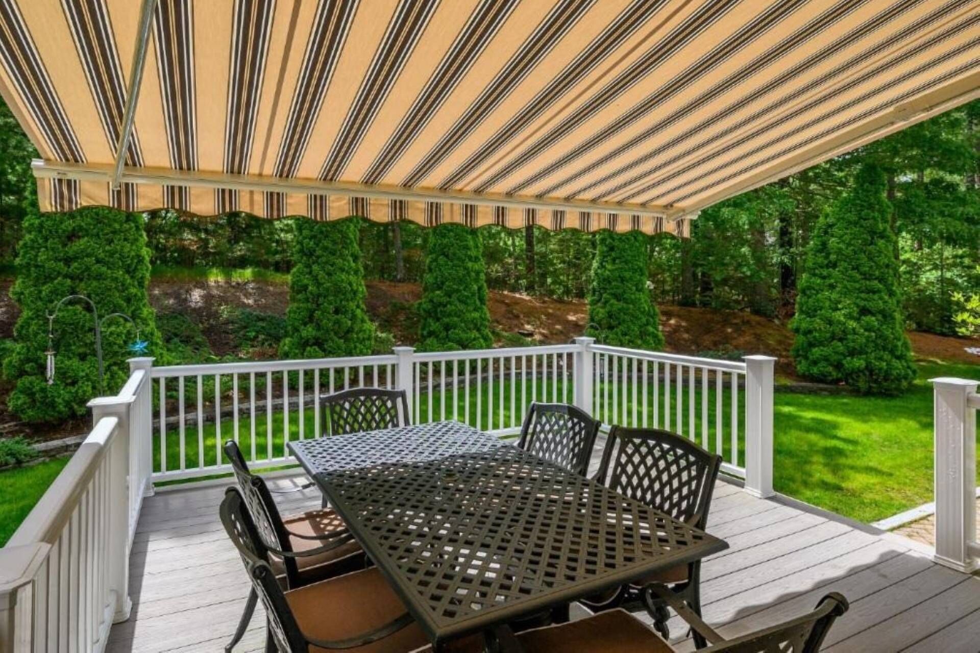 A covered patio with a table and chairs, surrounded by white railings and greenery.