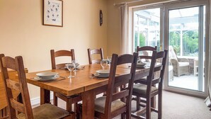 Une salle à manger avec une table et des chaises en bois, un tableau encadré au mur et une vue sur la verdure à travers la porte vitrée.