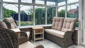 Une véranda meublée de meubles en osier, avec une table en bois et une vue sur le jardin.
