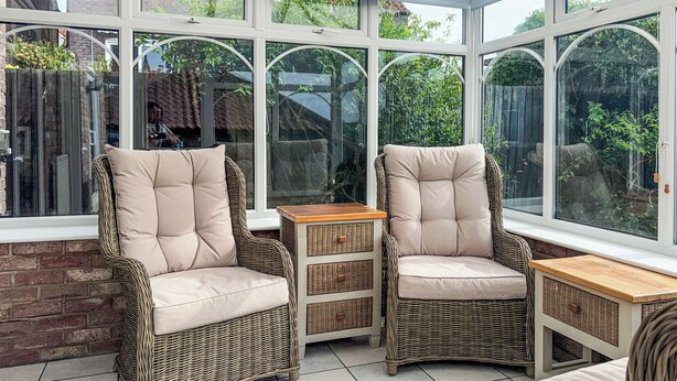 Une véranda meublée de mobilier en osier et dotée de grandes fenêtres.