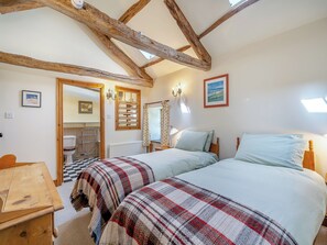 Une chambre avec deux lits, des poutres en bois au plafond, un radiateur et une fenêtre avec des rideaux.