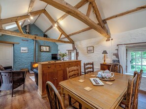 A rustic kitchen with exposed wooden beams, a stone wall, and a wooden dining table with chairs. - 2 bedroom accommodation in Carlisle (Carlisle)