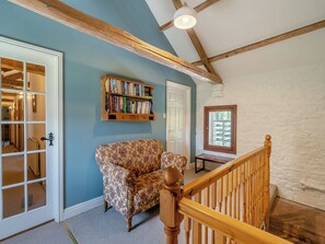 A room with a wooden staircase, a patterned armchair, a bookshelf, and a door leading to another room. - 2 bedroom accommodation in Carlisle (Carlisle)