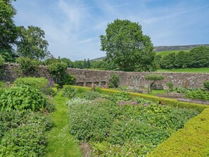 Un mur de pierre avec une serre, un jardin luxuriant et un grand arbre en arrière-plan.