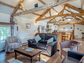 A rustic living room with exposed wooden beams, a leather sofa, a plaid armchair, and a dining area with wooden furniture. - 2 bedroom accommodation in Carlisle (Carlisle)