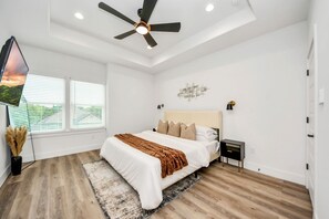 Une chambre à coucher moderne, dotée d’un grand lit, d’un ventilateur de plafond et offrant une vue sur l’extérieur par la fenêtre.