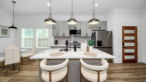 A modern kitchen with white cabinets, stainless steel appliances, and pendant lighting.
