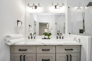Une salle de bain moderne avec deux vasques, un grand miroir et une douche.