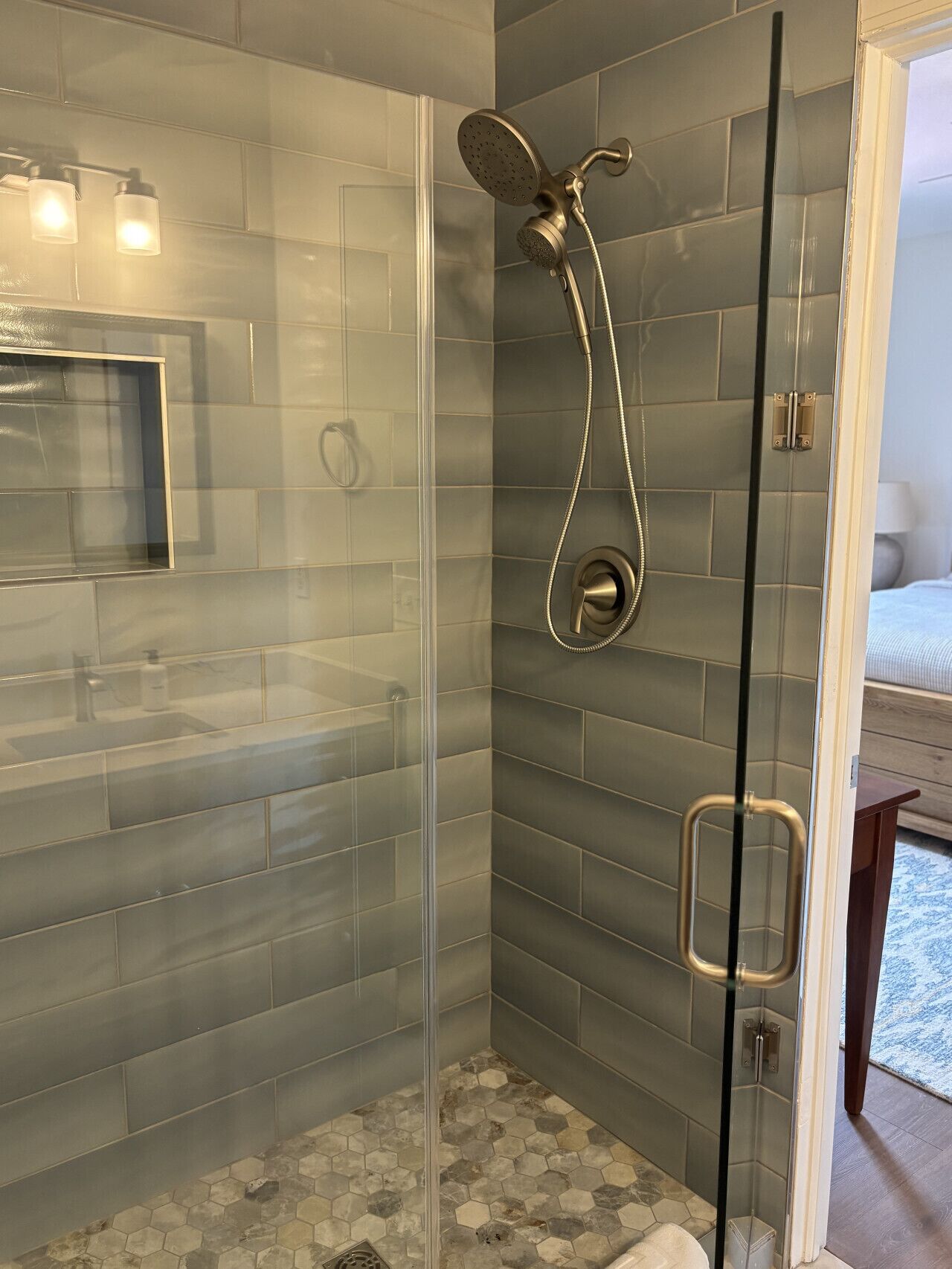 A modern shower with a glass door, grey tiles, and a handheld showerhead.
