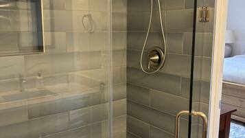 A modern shower with a glass door, grey tiles, and a handheld showerhead.