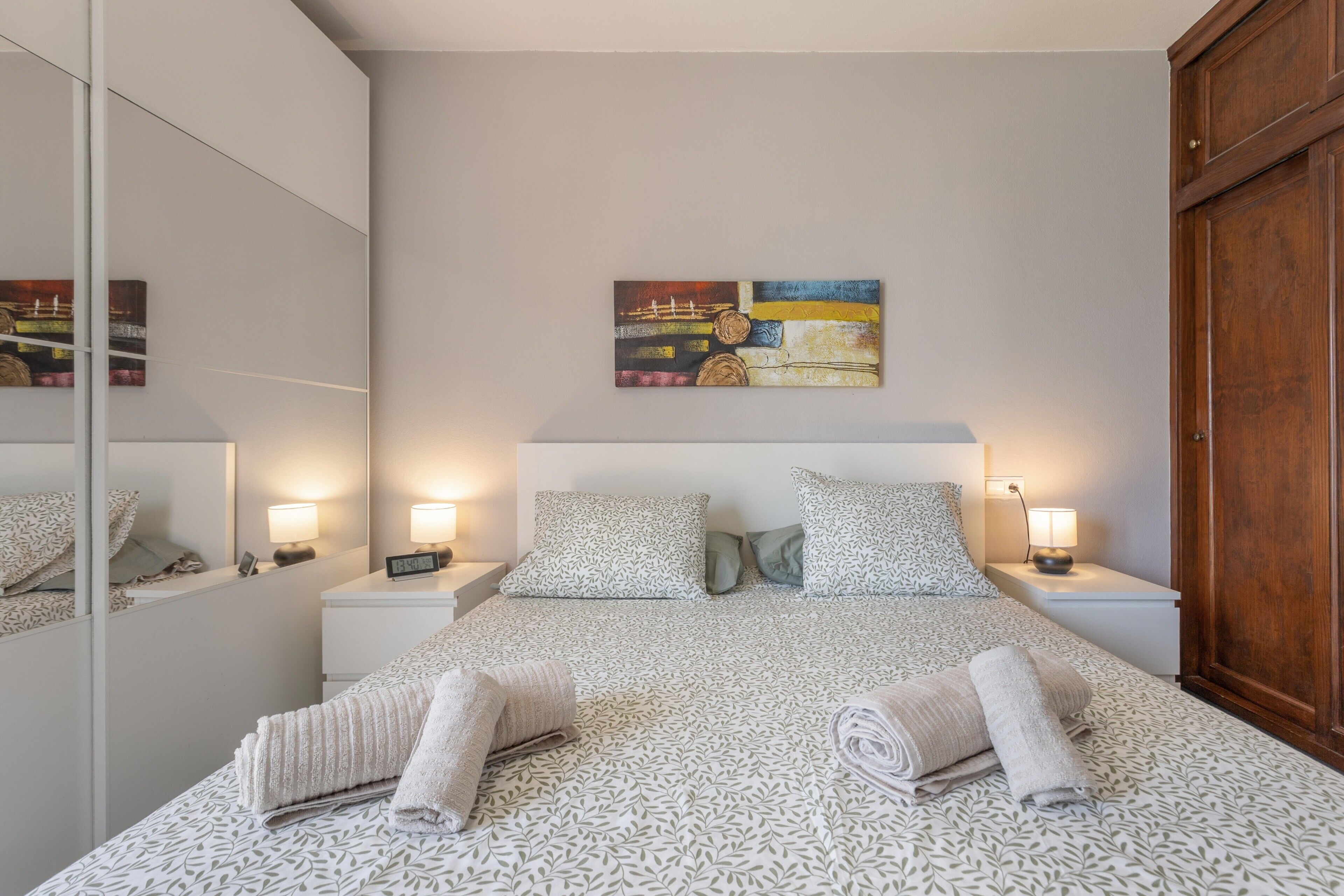 Een hotelkamer met een bed, nachtkastjes, een spiegel, een schilderij en een kledingkast.