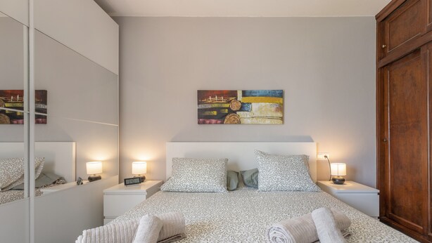 Una habitación de hotel con cama, mesitas de noche, un espejo, un cuadro y un armario.