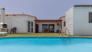 En swimmingpool med en patio, grill og et overdækket siddeområde.