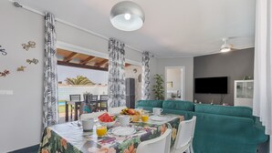Spiseområde med et bord dækket til morgenmad, en grøn sofa og et fjernsyn i stuen.