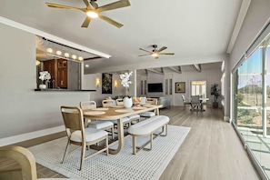 A spacious dining area with a high ceiling, ceiling fans, and a large window offering a view of the outdoors.