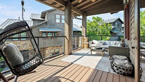A covered outdoor deck with a swing chair, a sofa set, and a stone fireplace. - Lake Travis Luxe Villa | 4BR | Pickleball | BBQ (Lake Travis)