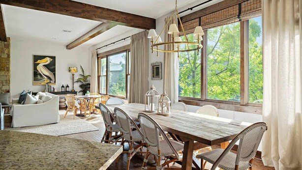 A dining area with a long wooden table, wicker chairs, and a hanging light fixture. - Lake Travis Luxe Villa | 4BR | Pickleball | BBQ (Lake Travis)
