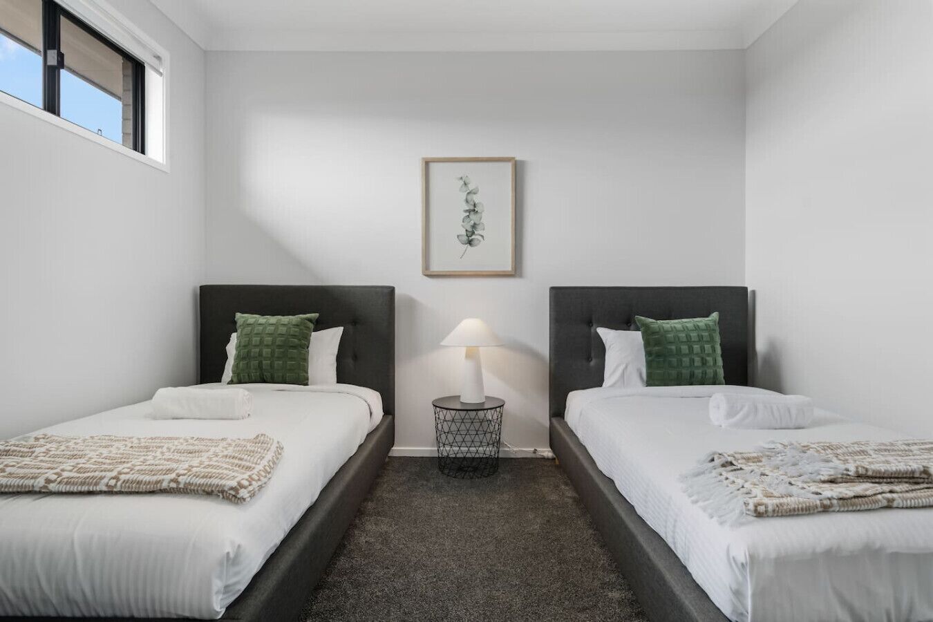 A hotel room with two beds, a small round table, a lamp, and a framed picture on the wall.