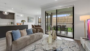 A modern living room with a sofa, a coffee table, and a dining area visible through glass doors. - 5BR Sleep 10 Family House | Patio Kitchen Garage (Park Ridge)