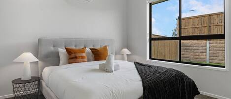 Une chambre avec un grand lit, deux lampes de chevet, une fenêtre donnant sur une clôture en bois et un climatiseur fixé au mur.