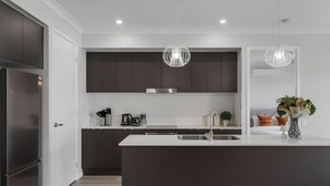 A modern kitchen with dark cabinets, a stainless steel refrigerator, a central island with a sink, and pendant lighting. - 5BR Sleep 10 Family House | Patio Kitchen Garage (Park Ridge)