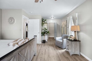 Un dormitorio con cama, cómoda, silla, lámpara y un reloj en la pared.