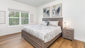 Une chambre à coucher avec un grand lit, une table de chevet, une fenêtre avec des stores et deux tableaux abstraits accrochés au mur.