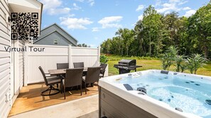 Un patio trasero con un jacuzzi, una mesa de comedor con sillas y una parrilla.