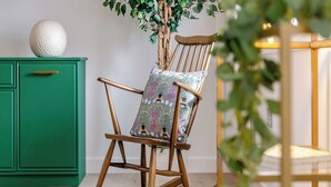 A rocking chair with a floral cushion, a green cabinet, and a plant in a room with wooden flooring.