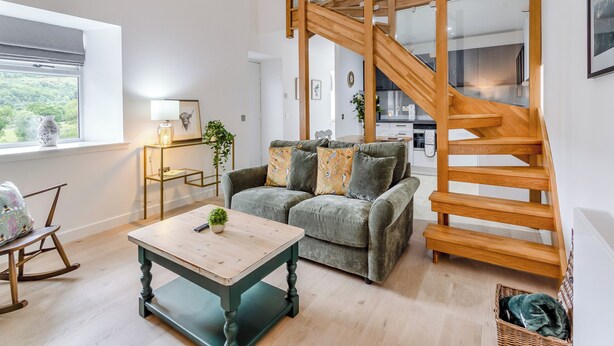 A modern living room with a wooden staircase, a sofa, a coffee table, and a view of the outdoors.