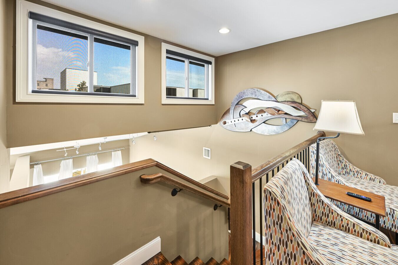 A staircase with a wooden handrail, a patterned chair, and a wall-mounted lamp.
