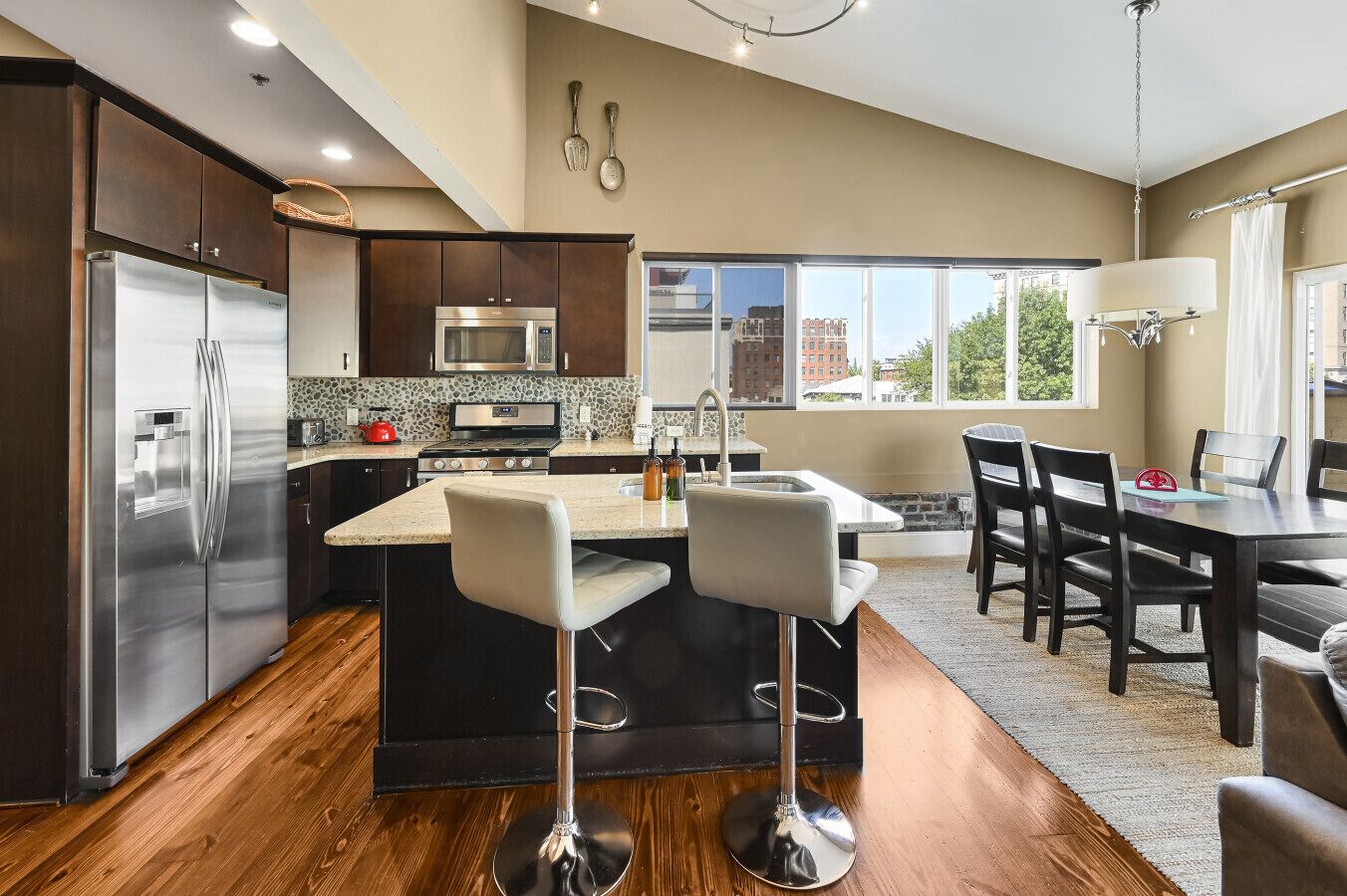 A modern kitchen with a central island, stainless steel appliances, and a dining area with a view.