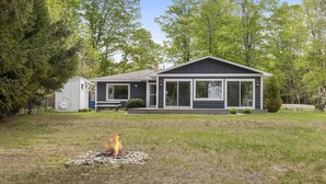 A modern two-story house with a large front porch, a fire pit in the yard, and a small shed to the left.