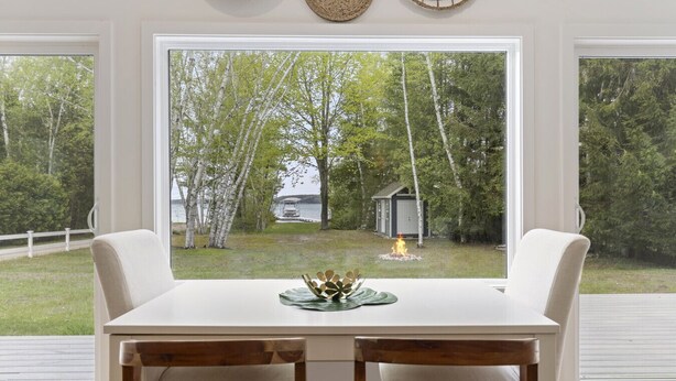A dining area with a table and chairs, a view of a backyard with trees and a small shed, and a fire in the distance.