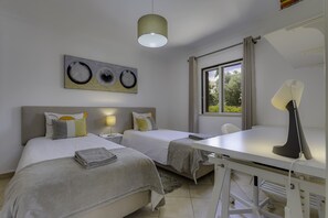 Ein Hotelzimmer mit zwei Betten, einem Schreibtisch, einer Lampe und einem Fenster mit Vorhängen.