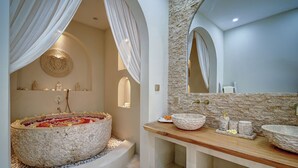 Une salle de bain dotée d’une grande baignoire en pierre, d’un meuble-lavabo en bois avec deux vasques et d’un mur en pierre.