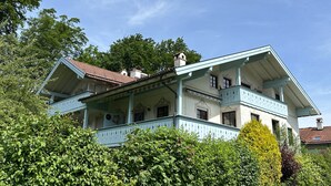 A large, two-story building with a balcony, surrounded by lush greenery. - Vacation apartment Zellerhorn 50 sqm, separate bedroom, south-facing balcony and underground garage (Aschau im Chiemgau)