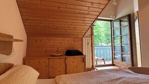 A bedroom with wooden ceiling, a bed, a dresser, and a window with a view of greenery. - Vacation apartment Zellerhorn 50 sqm, separate bedroom, south-facing balcony and underground garage (Aschau im Chiemgau)