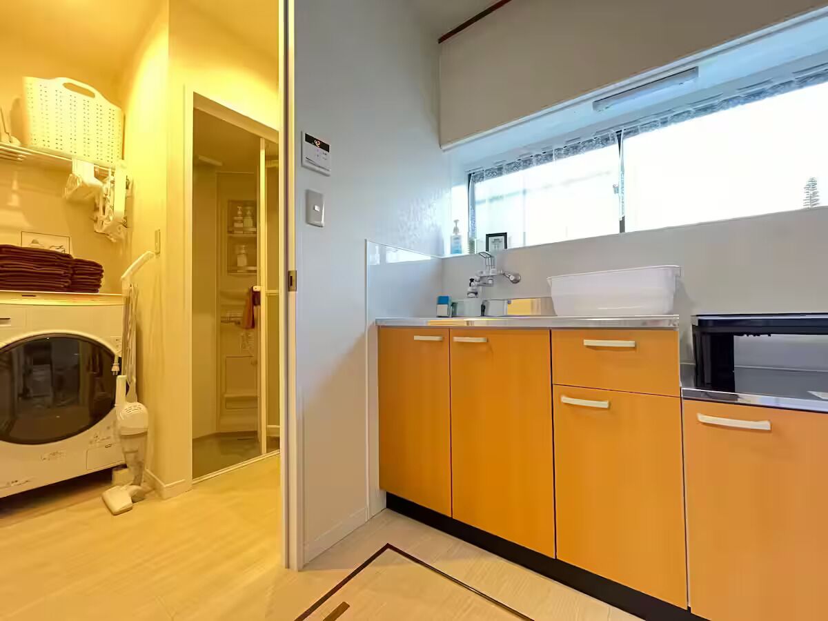 Une cuisine compacte avec des meubles en bois, un lave-linge et une fenêtre qui laisse entrer la lumière naturelle.