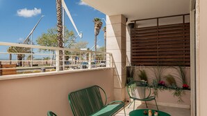A balcony with two green metal chairs, a small round table with decorative items, and a view of palm trees and a construction crane.