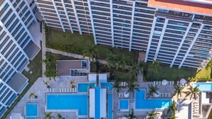 An aerial view of a resort with multiple swimming pools, a beach area, and high-rise buildings in the background. - Luxury 2BD beachfront condo 8 pools at Harbor 171 2BD Condo for rent in North Ho (Puerto Vallarta)
