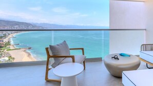 A balcony with a view of a beach and ocean, a wooden chair, a small white table, and a round ottoman. - Luxury 2BD beachfront condo 8 pools at Harbor 171 2BD Condo for rent in North Ho (Puerto Vallarta)