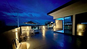Un espace extérieur aménagé en terrasse, doté d’un design moderne, comprenant un coin salon et un grand parasol.