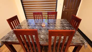 A dining table with six wooden chairs, a floral tablecloth, and a potted plant in the center.